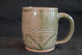 Green ceramic mug with decorative patterns on a dark background