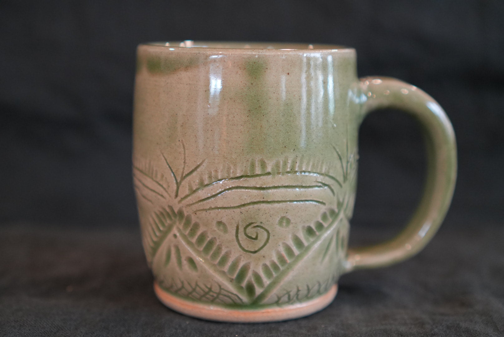Green ceramic mug with decorative patterns on a dark background