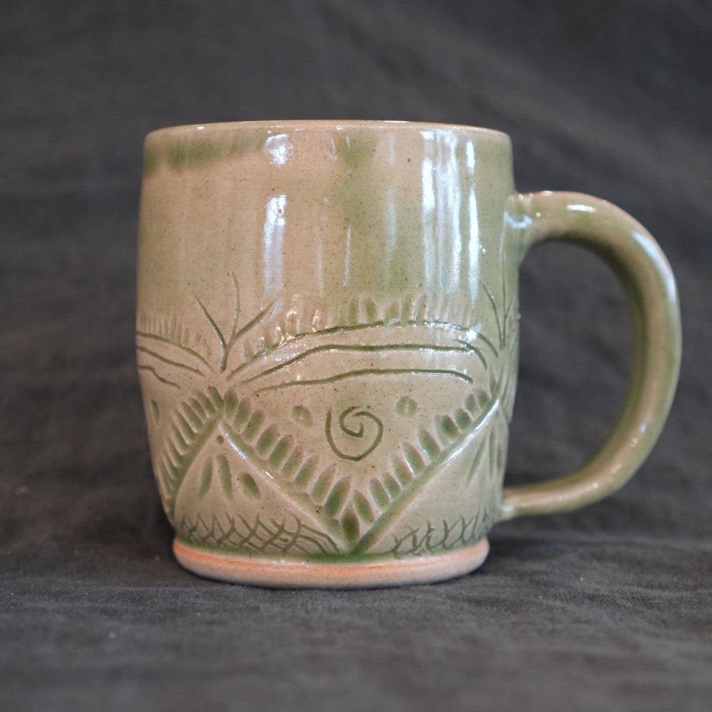 Green ceramic mug with carved patterns on a dark textured surface